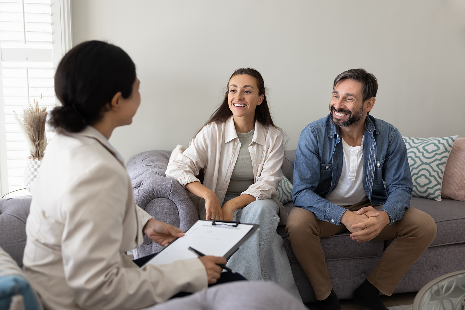 A couple sits smiling on a couch across from a professional.