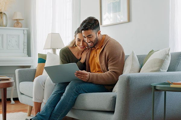couple sitting on a couch, looking at a laptop together
