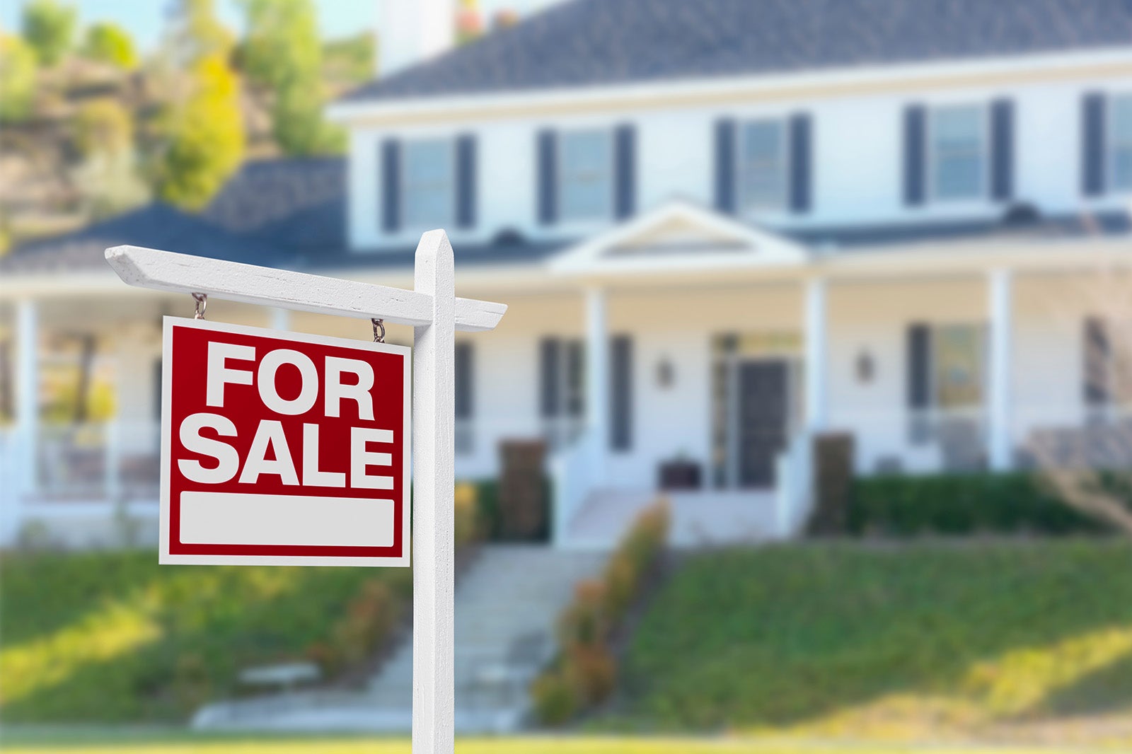A red and white for sale sign outside, in front of a white two story home.