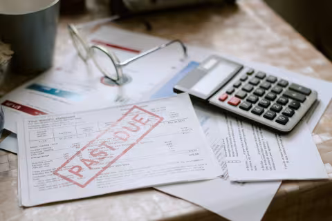 A pile of bills on a desk, with the top billing stamped "past due" next to a calculator.