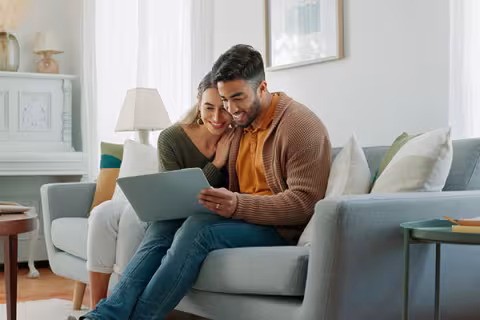 couple sitting on a couch, looking at a laptop together