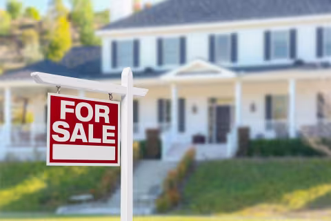 A red and white for sale sign outside, in front of a white two story home.